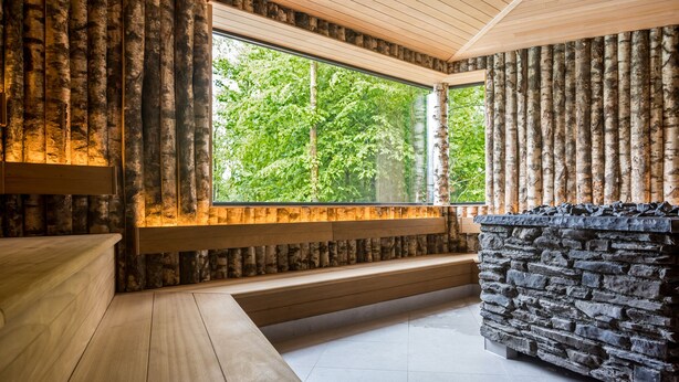 A room with a large window, wooden bench seating, and a stone fireplace. - Dormio Resort Maastricht (Maastricht)