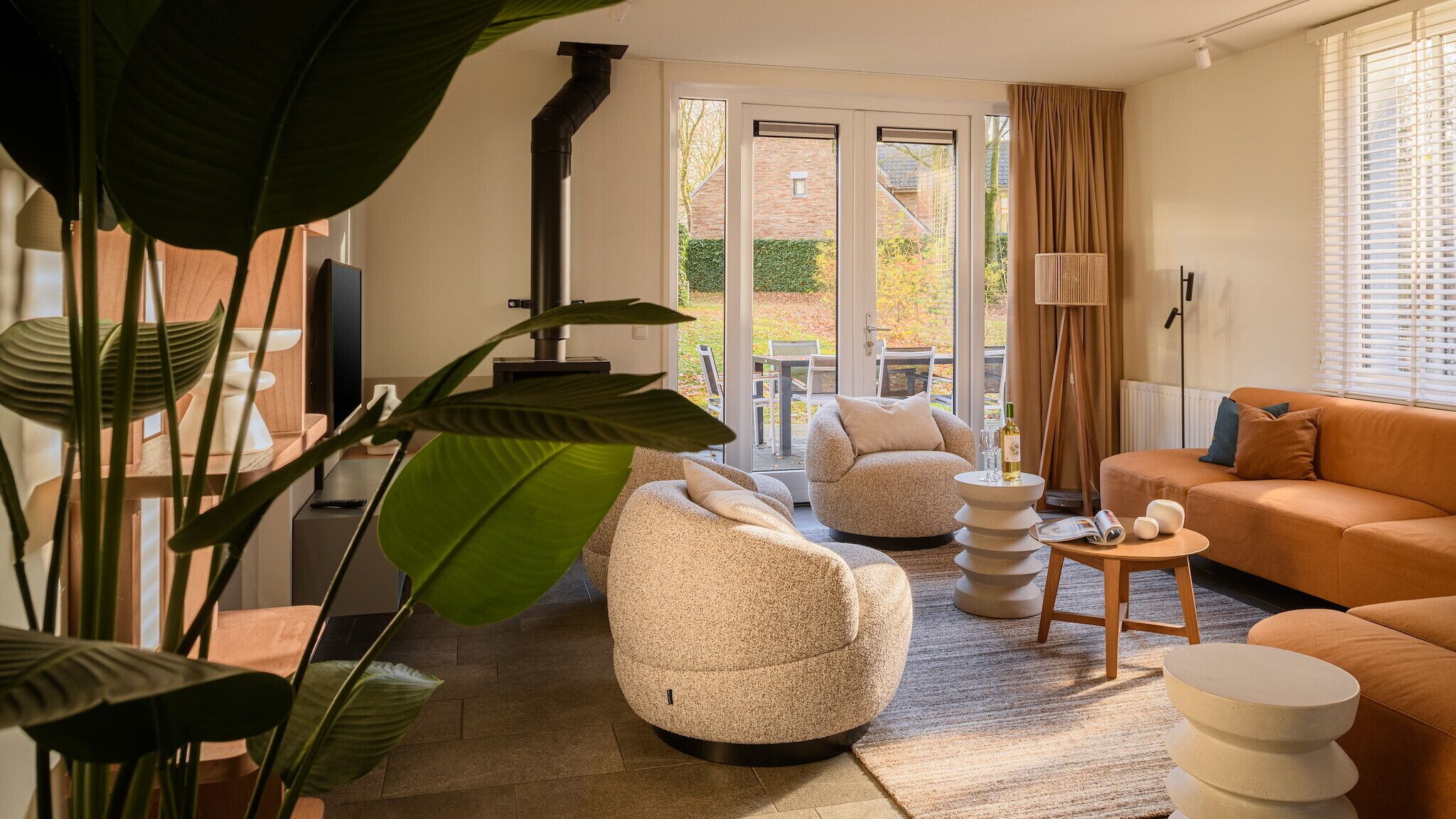 Un salon moderne avec un canapé, deux fauteuils en forme de poire, une table basse et un lampadaire. Une grande fenêtre, ornée de rideaux, offre une vue sur l’extérieur.
