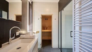 A modern bathroom with a large mirror, a white sink, and a wooden sauna door.