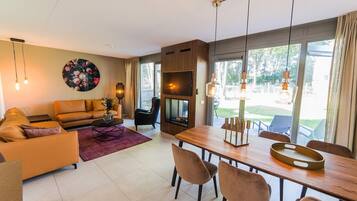 A modern living room with a sofa, coffee table, and dining area with chairs. There is a TV and a fireplace.