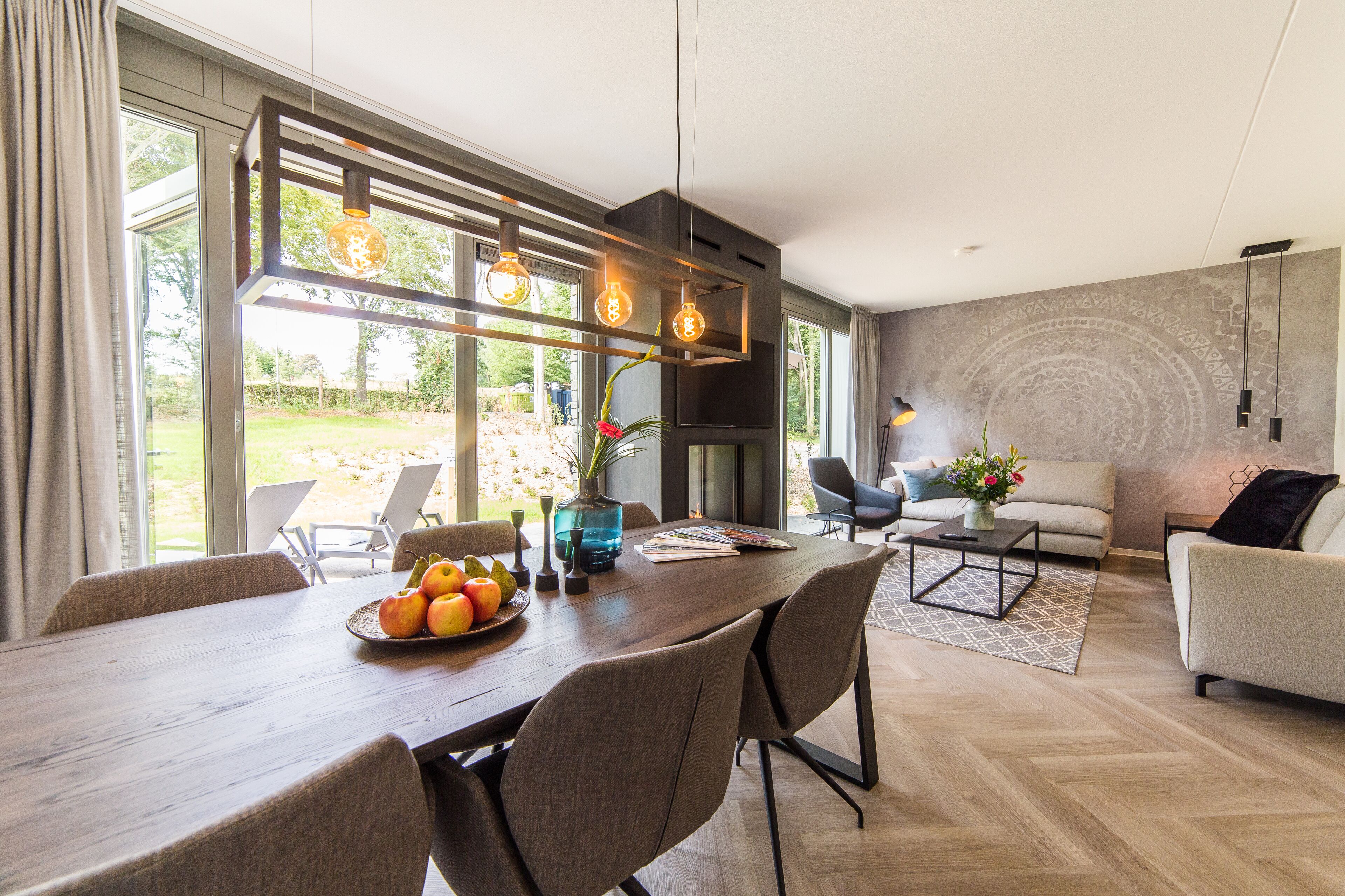 A modern living room with a wooden dining table, comfortable seating, and a large window offering a view of the outdoors.