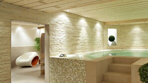 A modern spa area with a hot tub, stone walls, and a wooden ceiling.