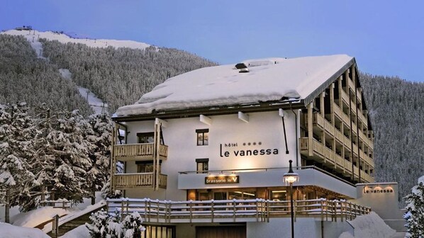Hotel Le vanessa med et sneklædt tag, en balkon og et skilt, der angiver en brasserie.