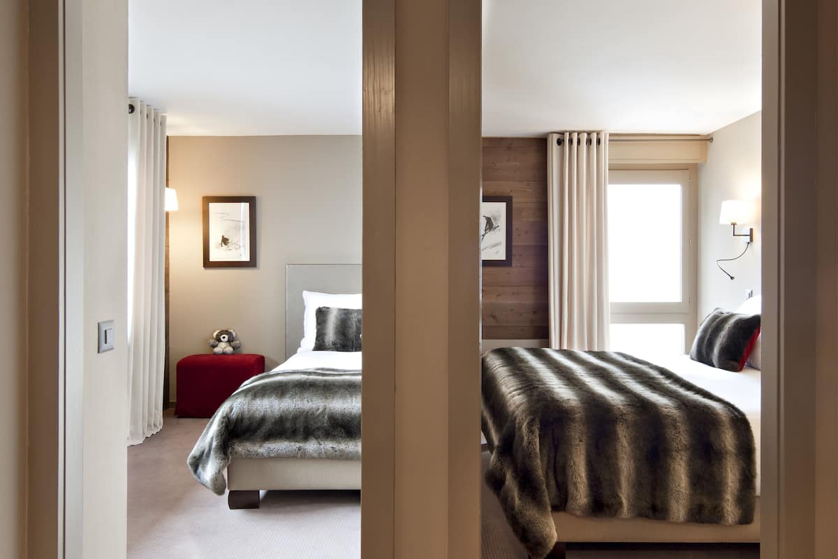 A hotel room with a large bed, a red chair, and a small table with a teddy bear.