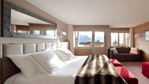 A hotel room with a bed, a red sofa, a wooden wall, and a window with a mountain view.