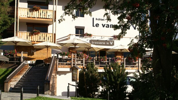 A hotel with outdoor seating, a staircase, and a sign reading "brasserie le V".