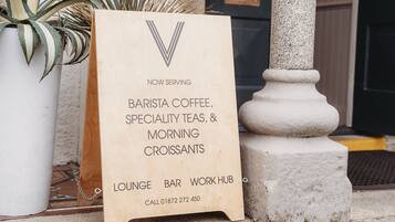 Un letrero de madera que anuncia café de barista, tés especiales y cruasanes para el desayuno, con un número de contacto.
