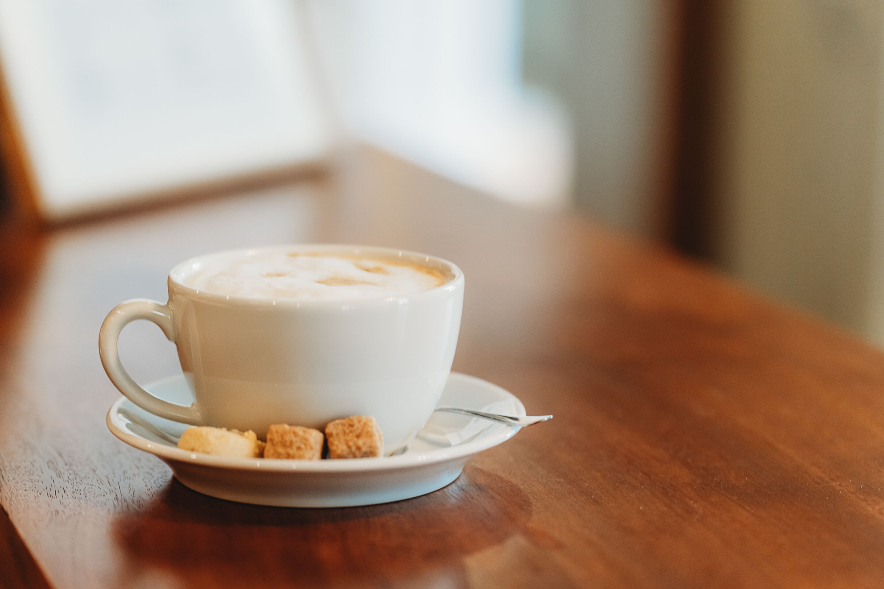 A white cup of coffee with a saucer and a spoon on a wooden table.