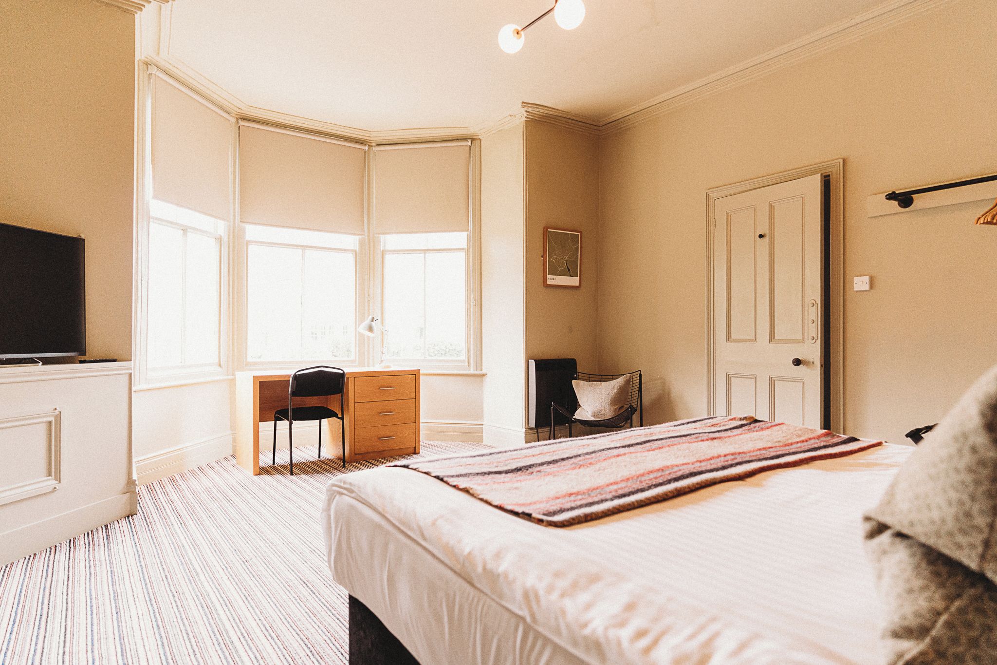 A bedroom with a bed, a desk, a chair, a television, and a door.