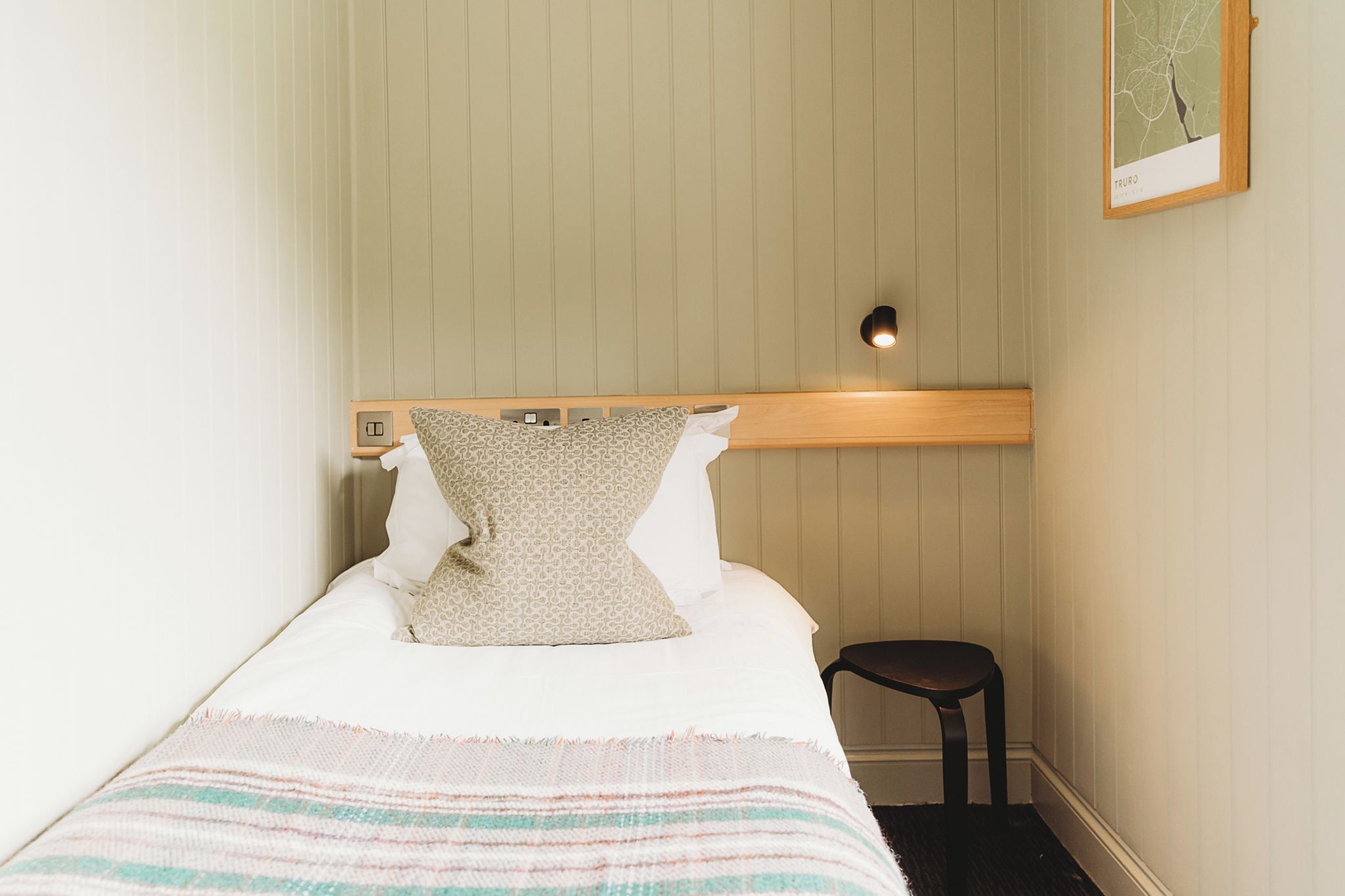 A single bed with a headboard, a bedside table, and a wall-mounted light fixture.