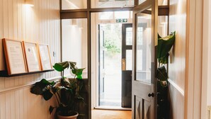 A hallway with a potted plant, framed certificates on the wall, and a door leading to an outdoor area.