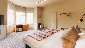 A bedroom with a large bed, a desk, and a chair. There are windows, a door, and a light fixture.