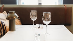 A dining table with two wine glasses and a candle holder, set against a window with a view of buildings.
