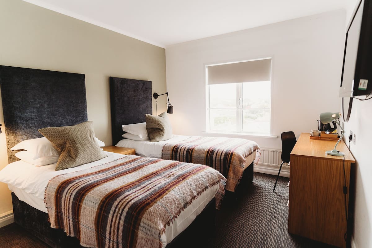 Ett hotellrum med två sängar, ett skrivbord, en stol och ett fönster.