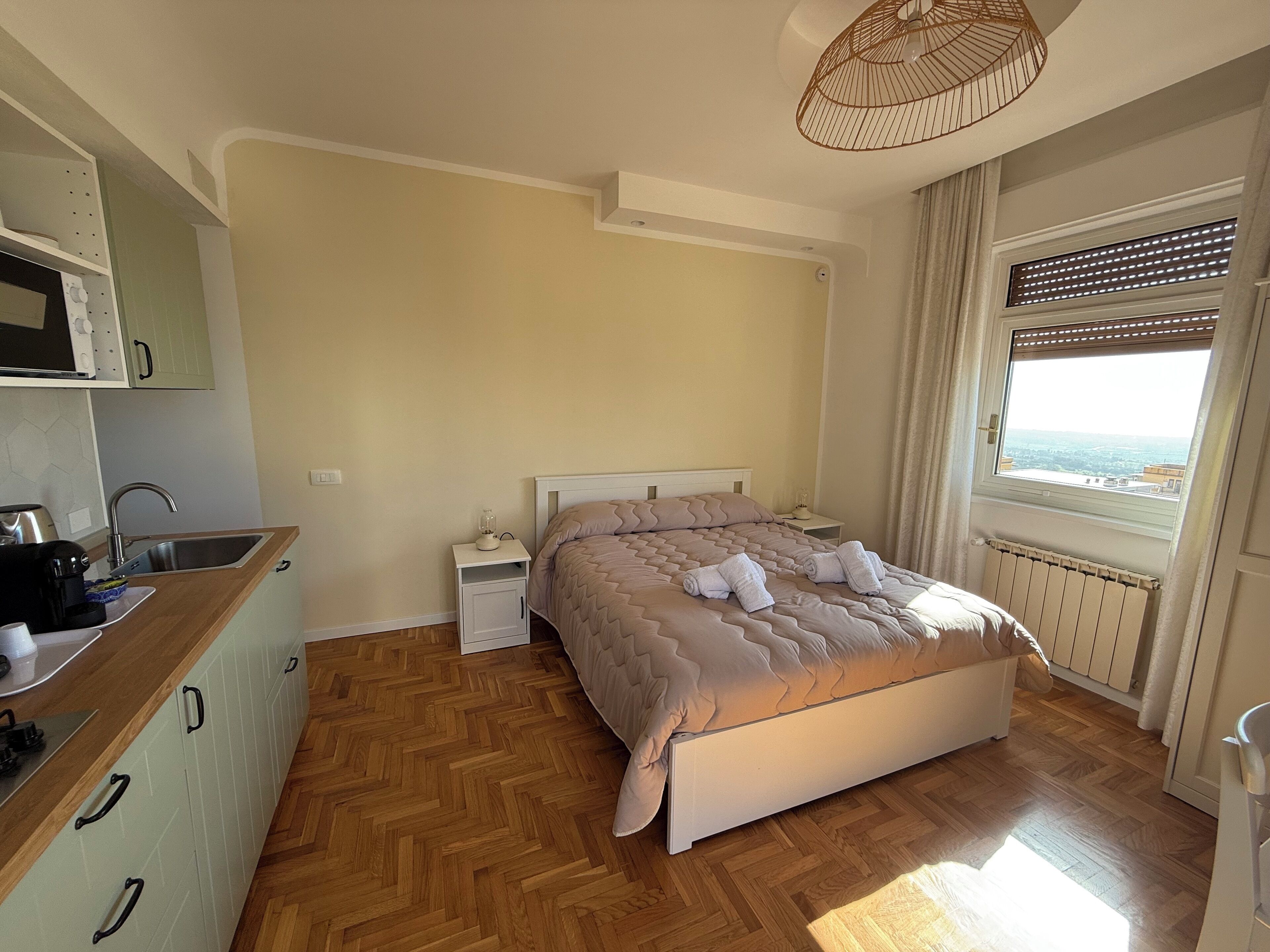 Een slaapkamer met een bed, nachtkastje, keukenhoek met een spoelbak en een magnetron.