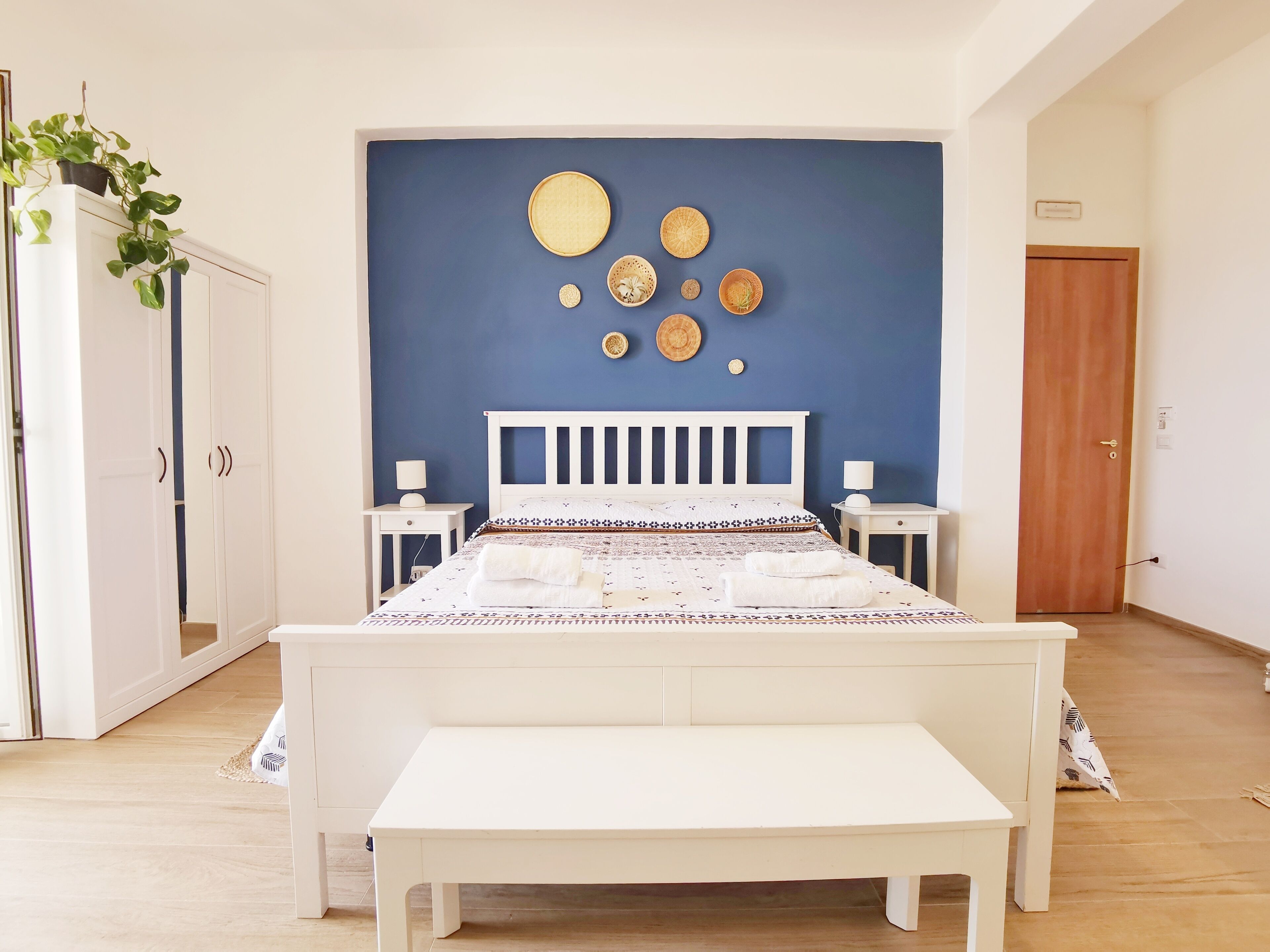 A bedroom with a bed, bedside tables, a bench, a wardrobe, and decorative wall art.