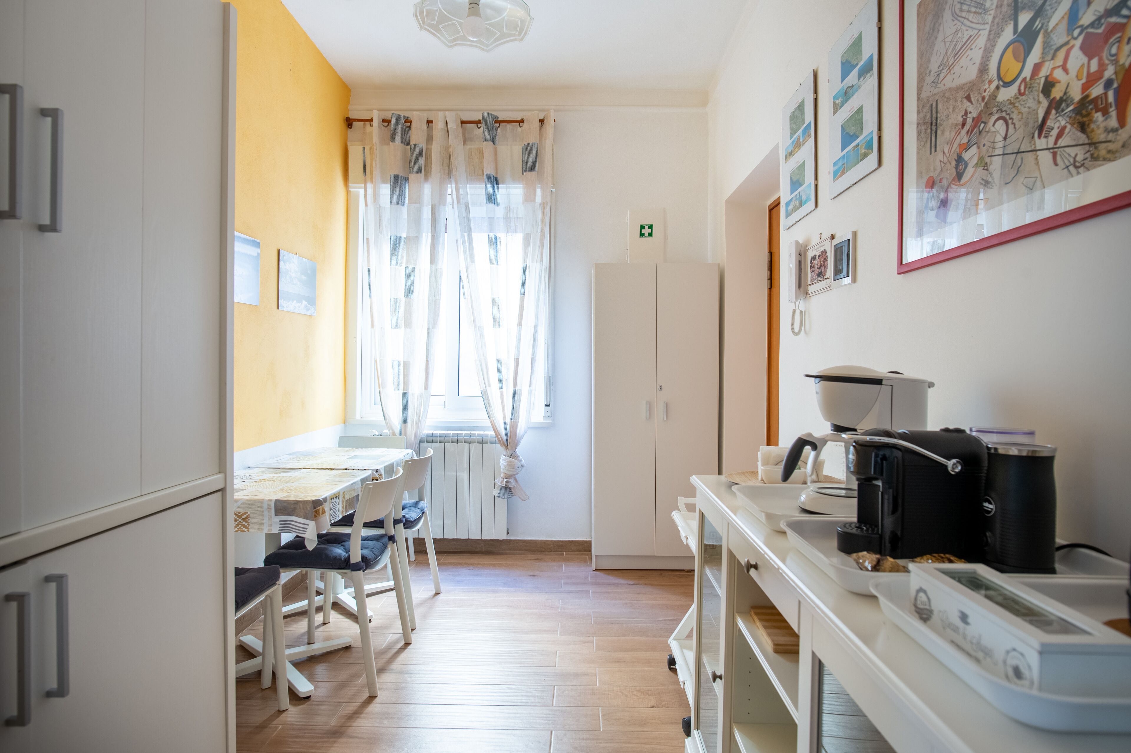 Una cocina compacta con una mesa de comedor, sillas, un refrigerador, una cafetera y un microondas.