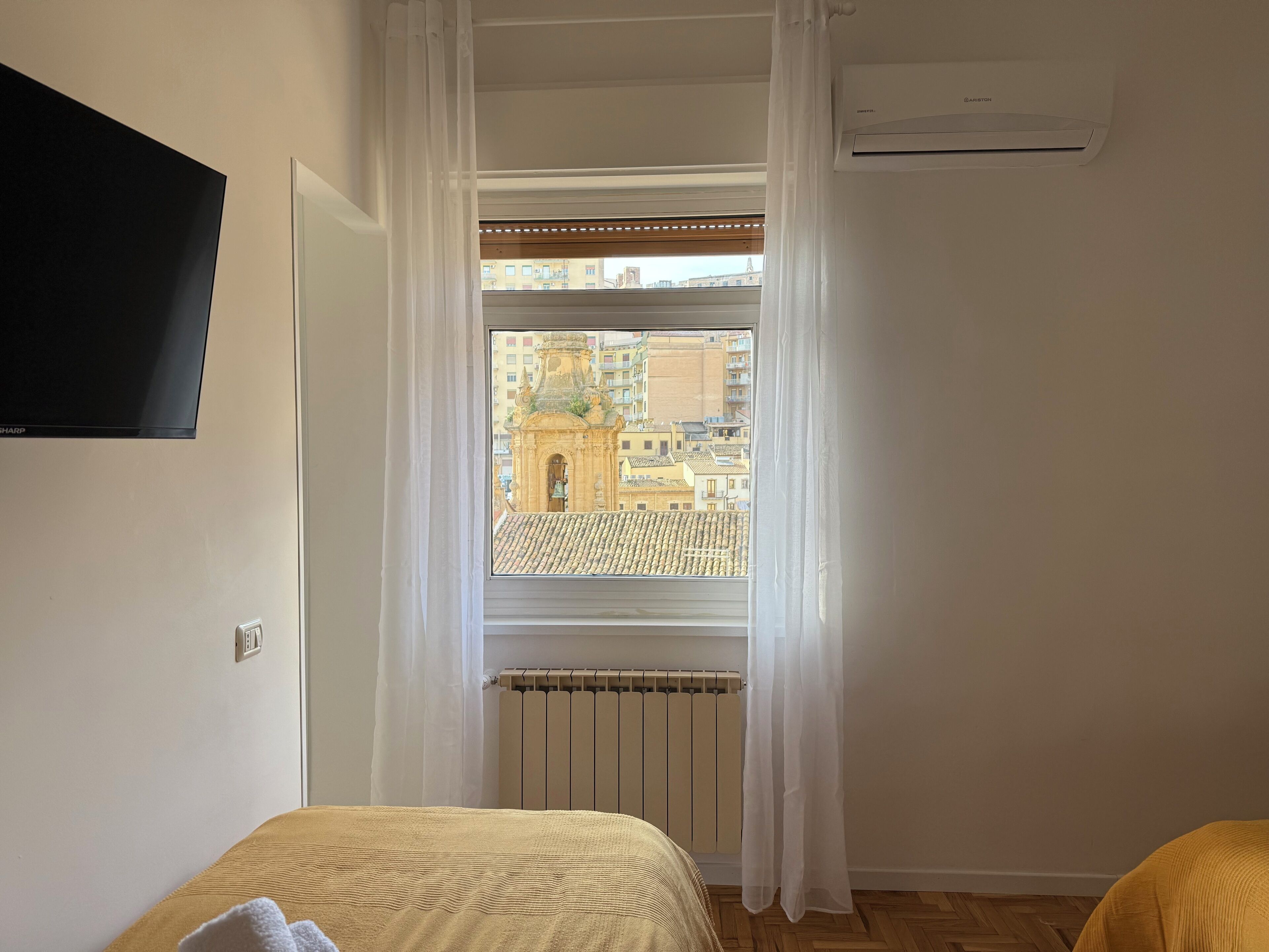 Habitación de hotel con cama, ventana con cortinas, aire acondicionado y vistas a edificios.