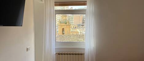 Habitación de hotel con cama, ventana con cortinas, aire acondicionado y vistas a edificios.