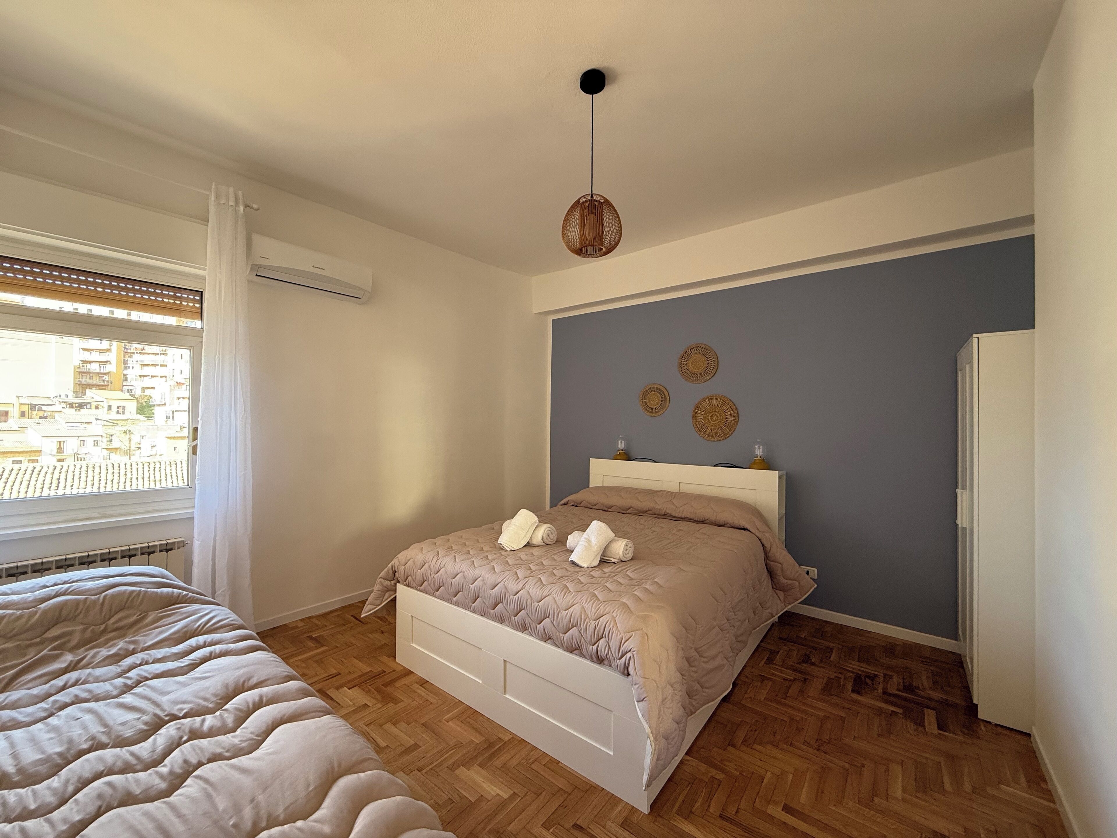 A bedroom with a bed, a window with blinds, a hanging light fixture, and a wall with decorative plates.