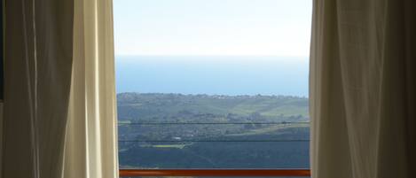 Vista a través de una ventana con cortinas, mostrando un paisaje con colinas y un horizonte lejano.