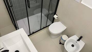 A modern bathroom with a glass-enclosed shower, a toilet, a bidet, and a sink.