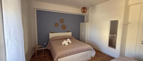 A bedroom with a bed, a wardrobe, a mirror, and a small table.