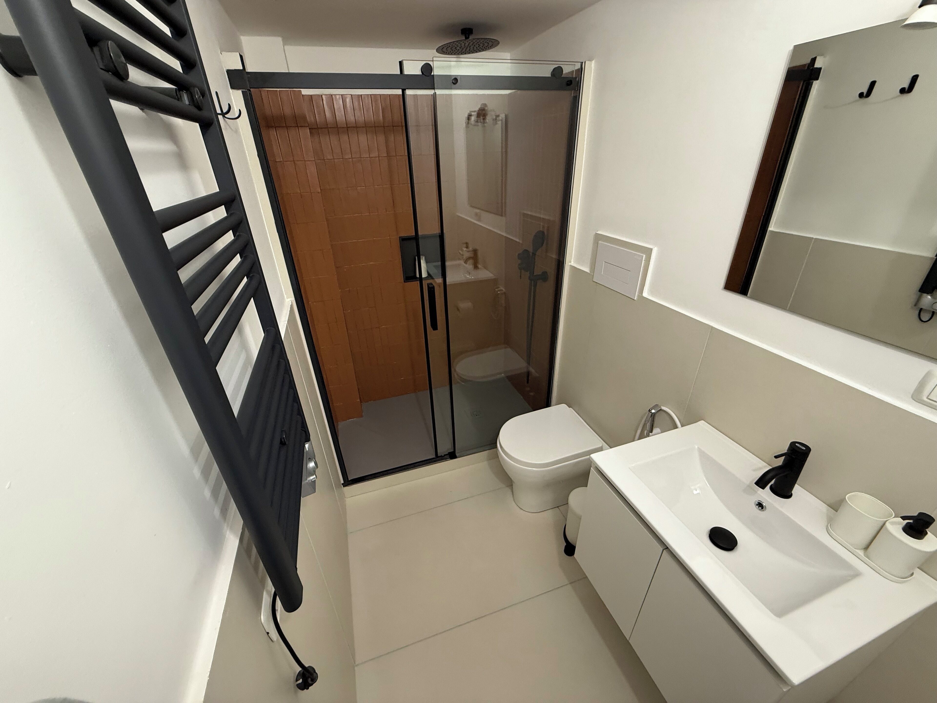 Une salle de bain moderne avec une douche à parois de verre, des toilettes blanches et un lavabo blanc avec un miroir au-dessus.