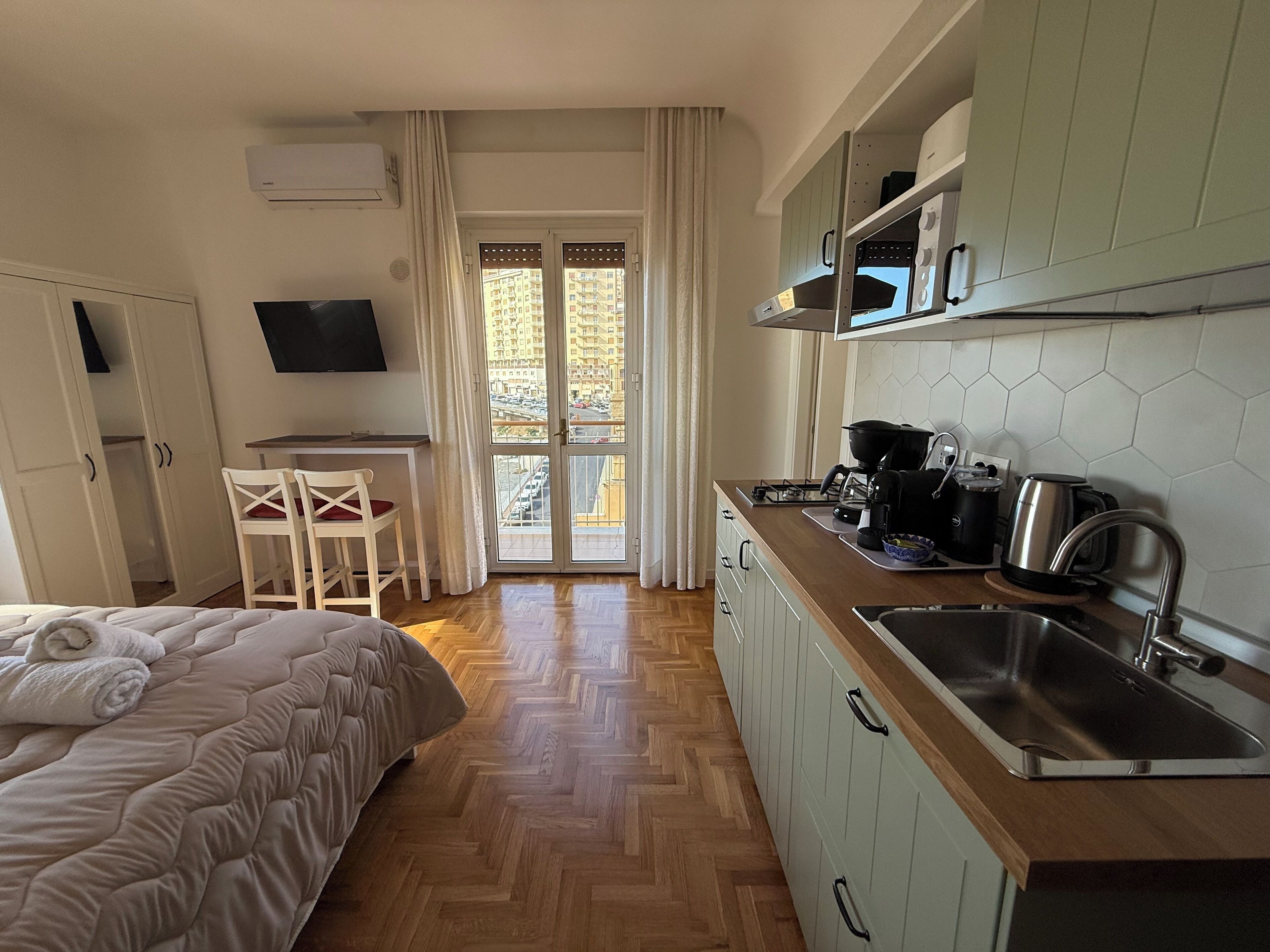 Habitación de hotel compacta con cama, un pequeño comedor, kitchenette y vistas a través de una puerta de cristal.