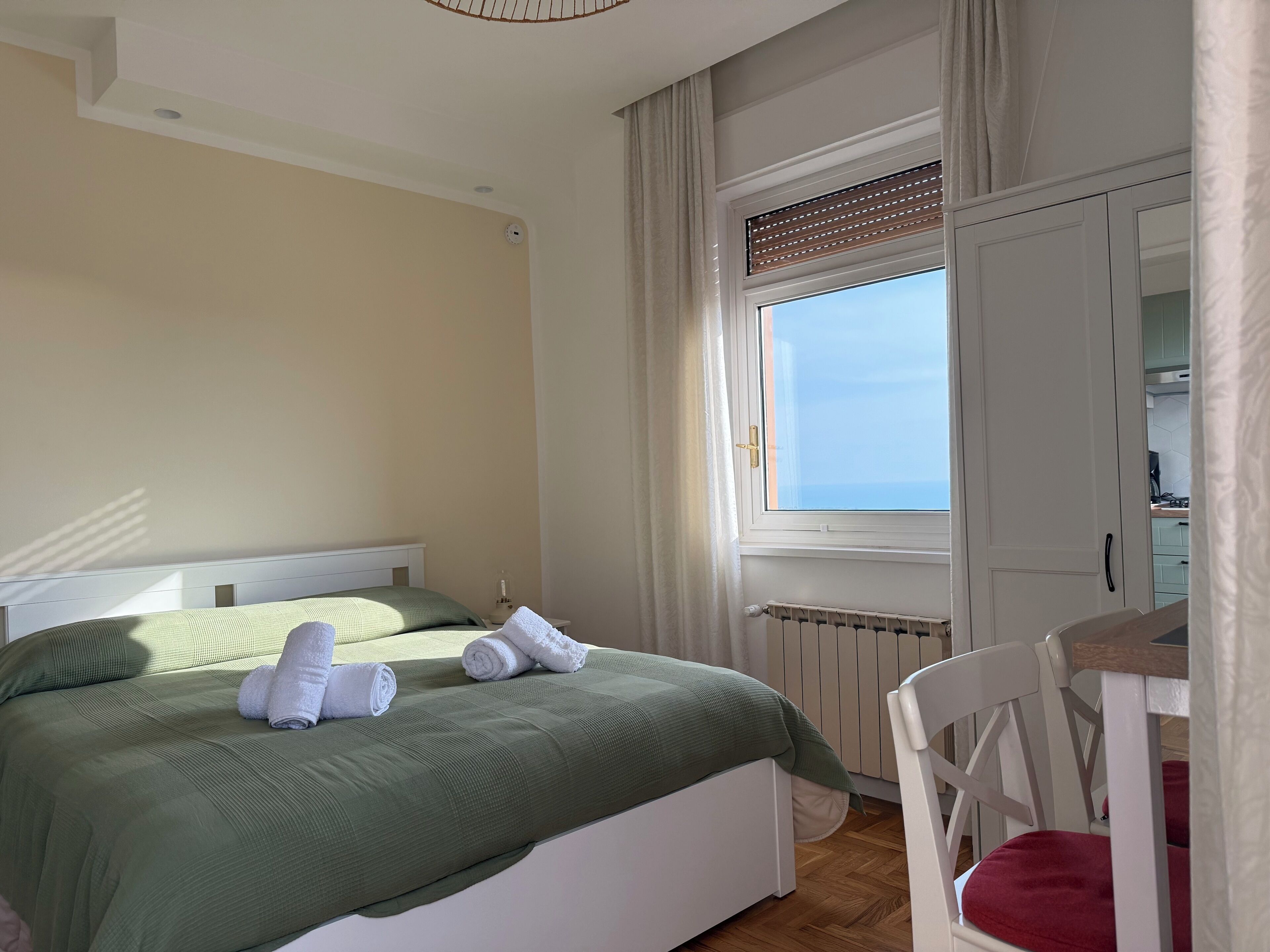 Un dormitorio con cama, ventana, radiador y una silla.