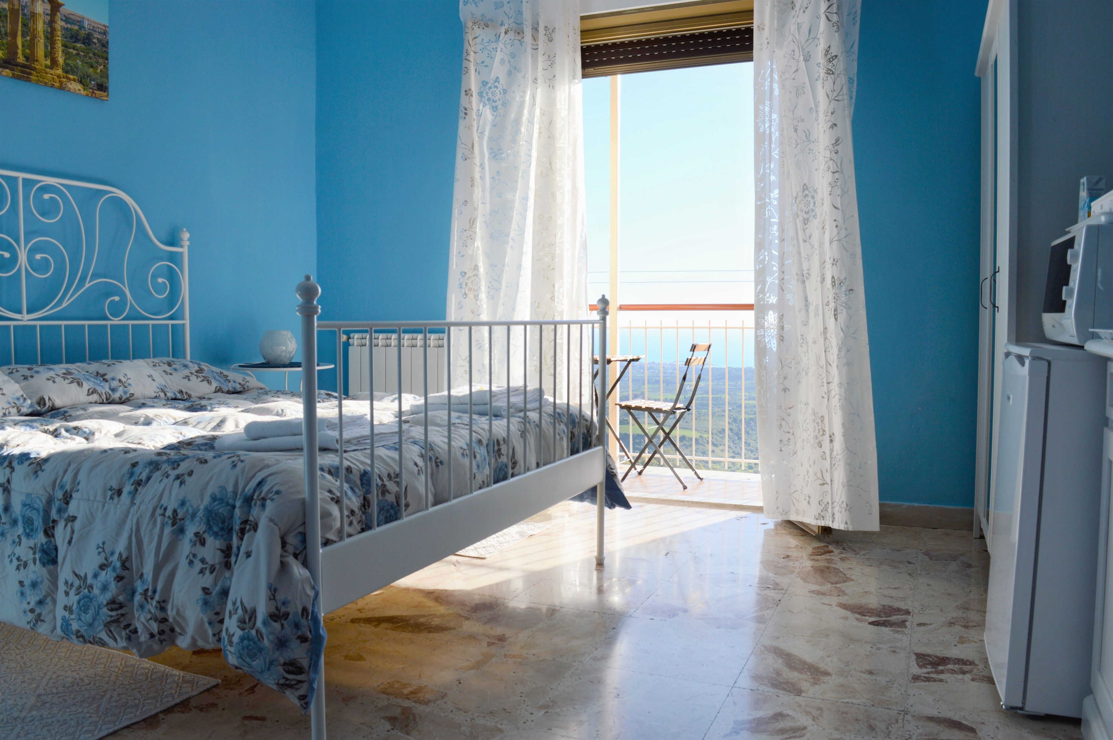A bedroom with a bed, a chair, a window with curtains, and a view of the sea.