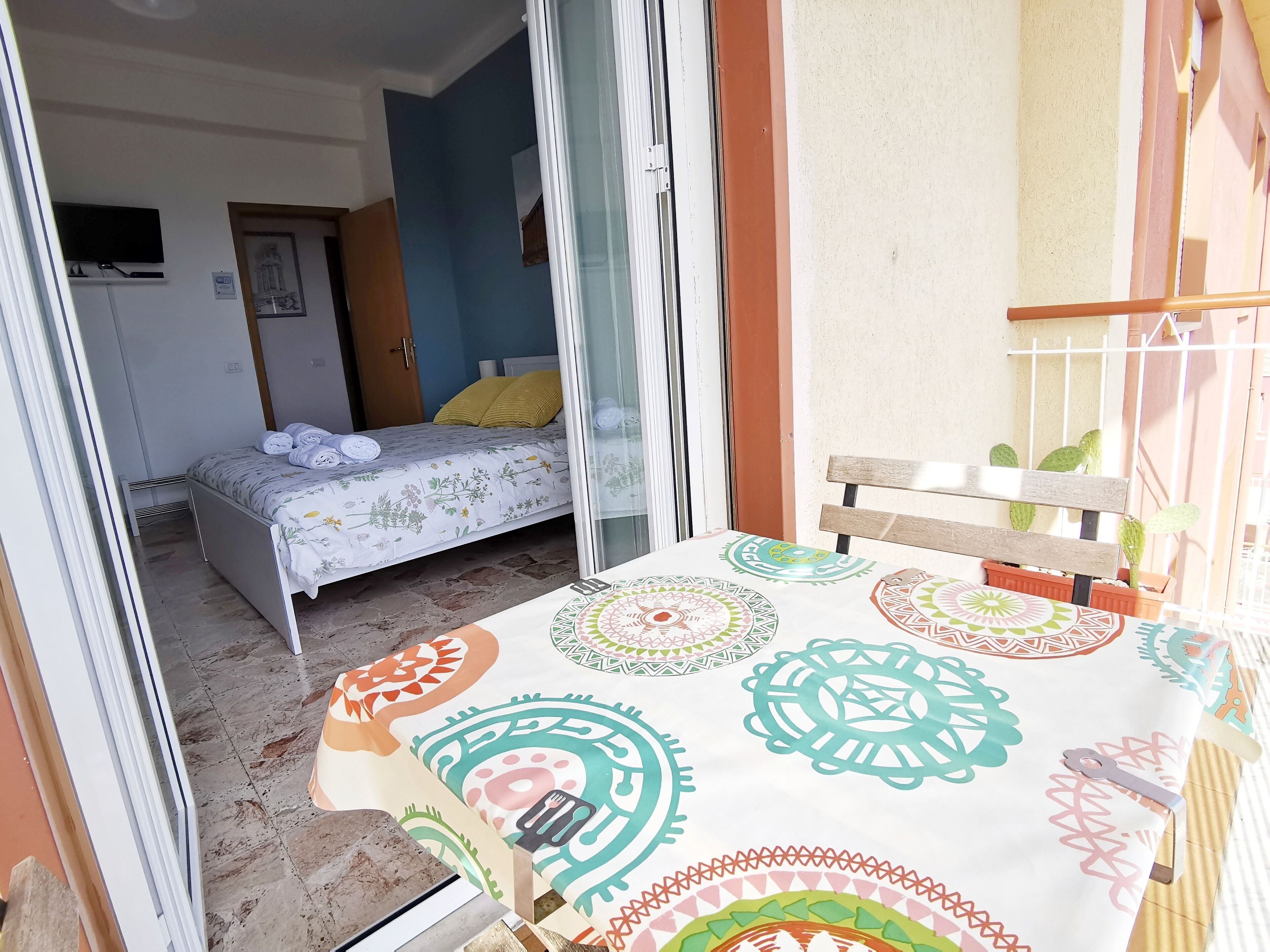 Un dormitorio con cama, ventana y una mesa con mantel estampado.