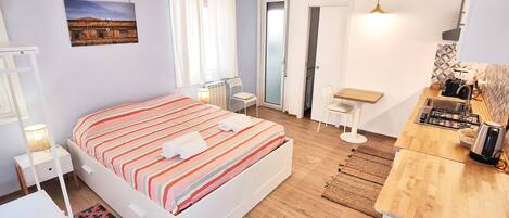 A bedroom with a bed, bedside tables, a small desk, a radiator, and a window with curtains.