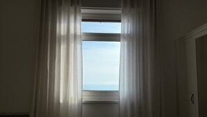 Una habitación con ventana cubierta por cortinas translúcidas, un radiador y una puerta.