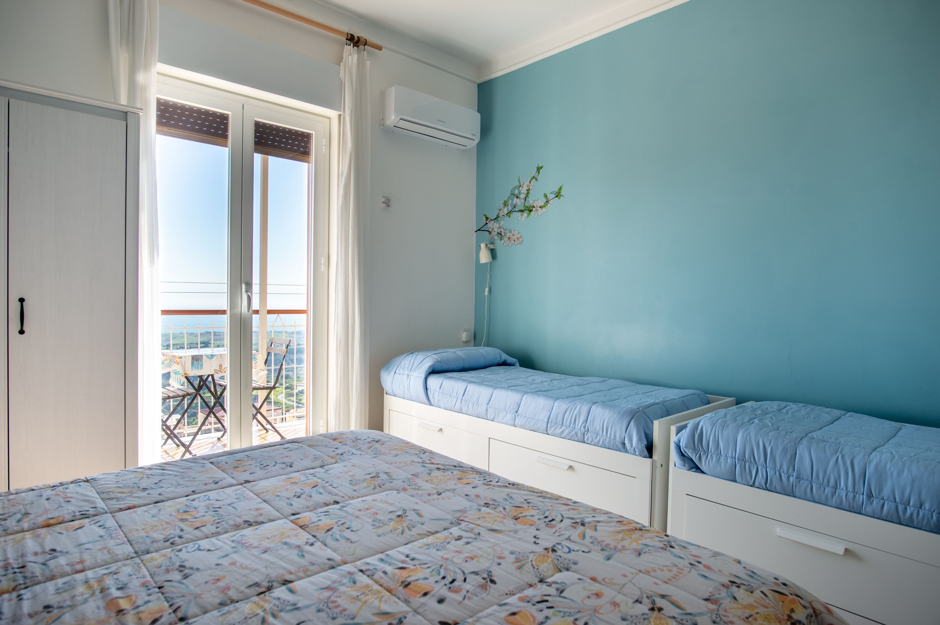 A bedroom with two beds, a balcony, and an air conditioning unit.