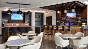 A modern bar area with multiple seating options, including round tables and bar stools. There are televisions mounted on the walls, and a variety of bottles and glasses are displayed on shelves. - Hyatt Place Edmonton-West (Edmonton)