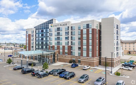A multi-story hotel with a modern design, featuring a glass entrance and a parking lot with several cars.