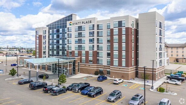 A multi-story hotel with a modern design, featuring a glass entrance and a parking lot with several cars. - Hyatt Place Edmonton-West (Edmonton)