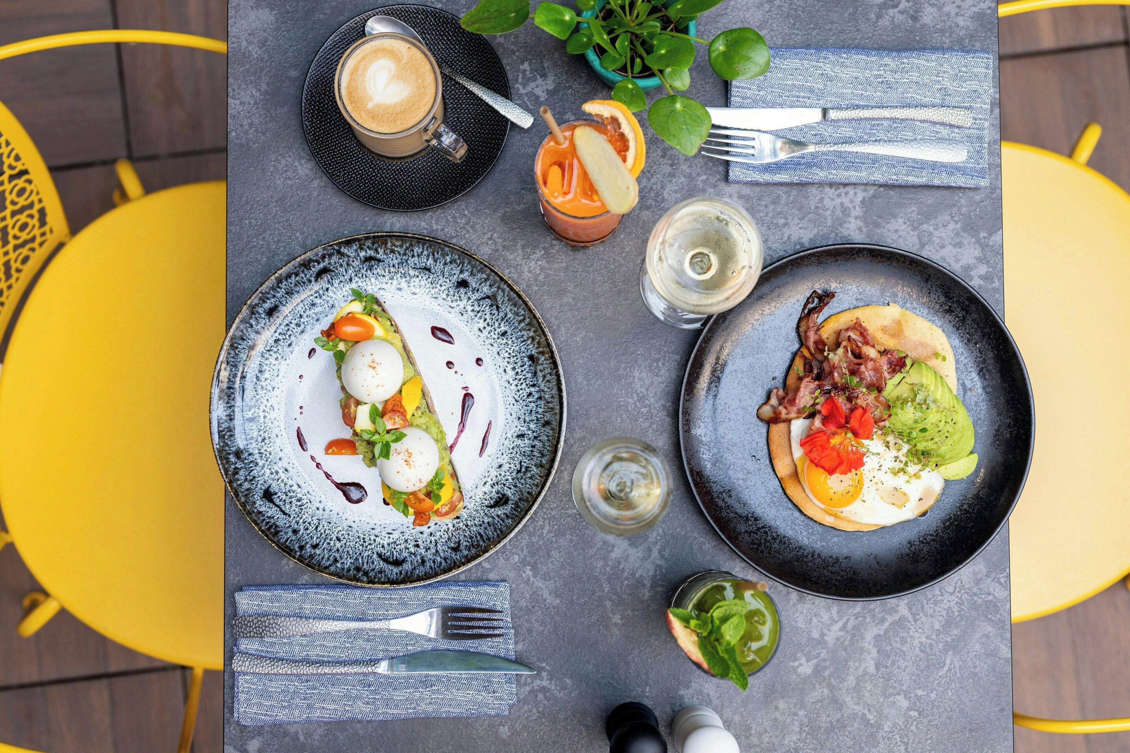 A dining table with two plates of food, a coffee cup, a glass of water, and a small plant.