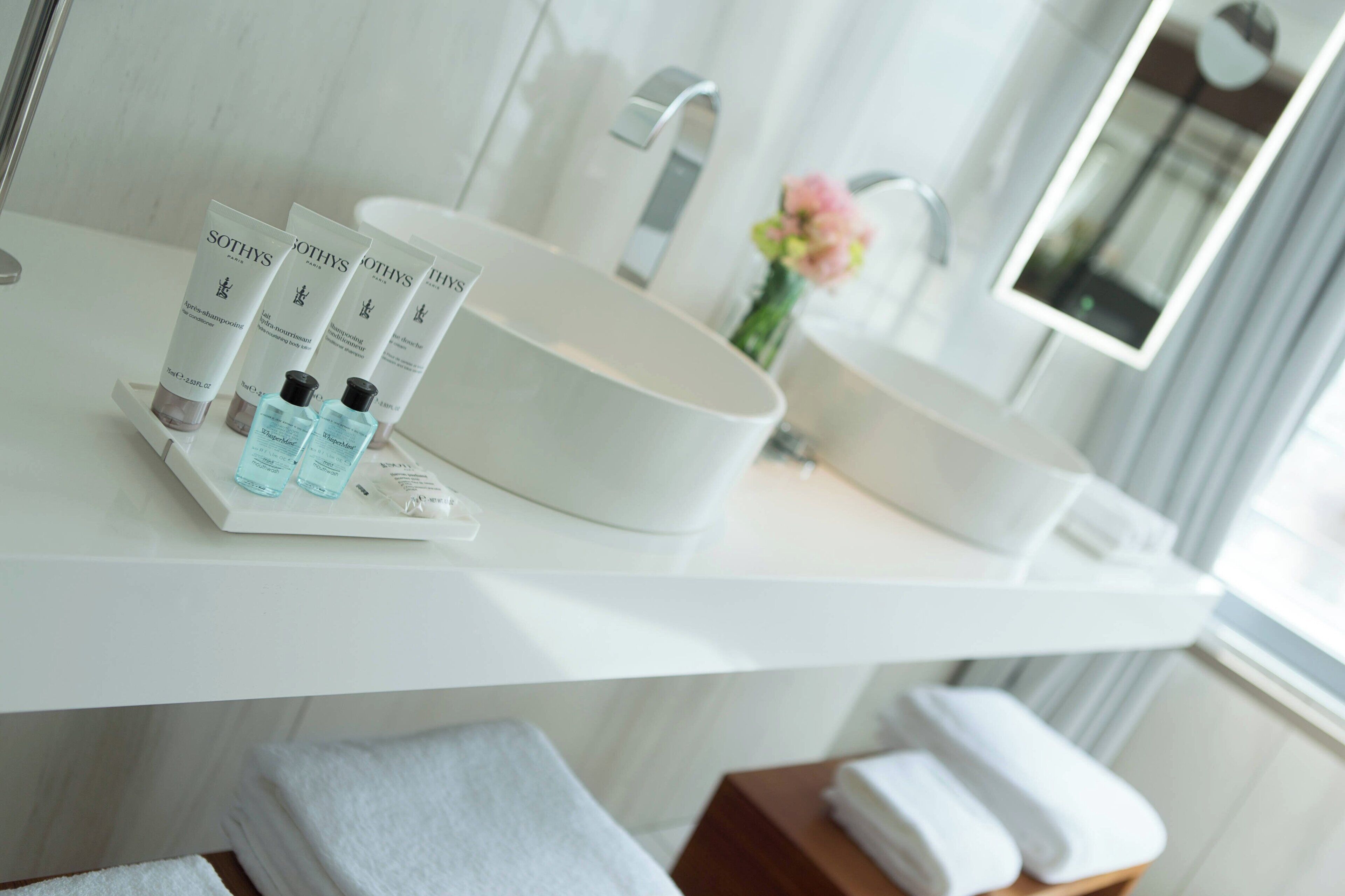 A modern bathroom with a large white sink, a mirror, and toiletries on the countertop.