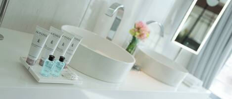 A modern bathroom with a large white sink, a mirror, and toiletries on the countertop.