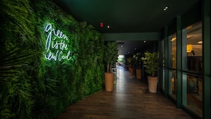 A hallway with a green wall, a neon sign, and potted plants. - Renaissance Paris Republique Hotel (Paris)