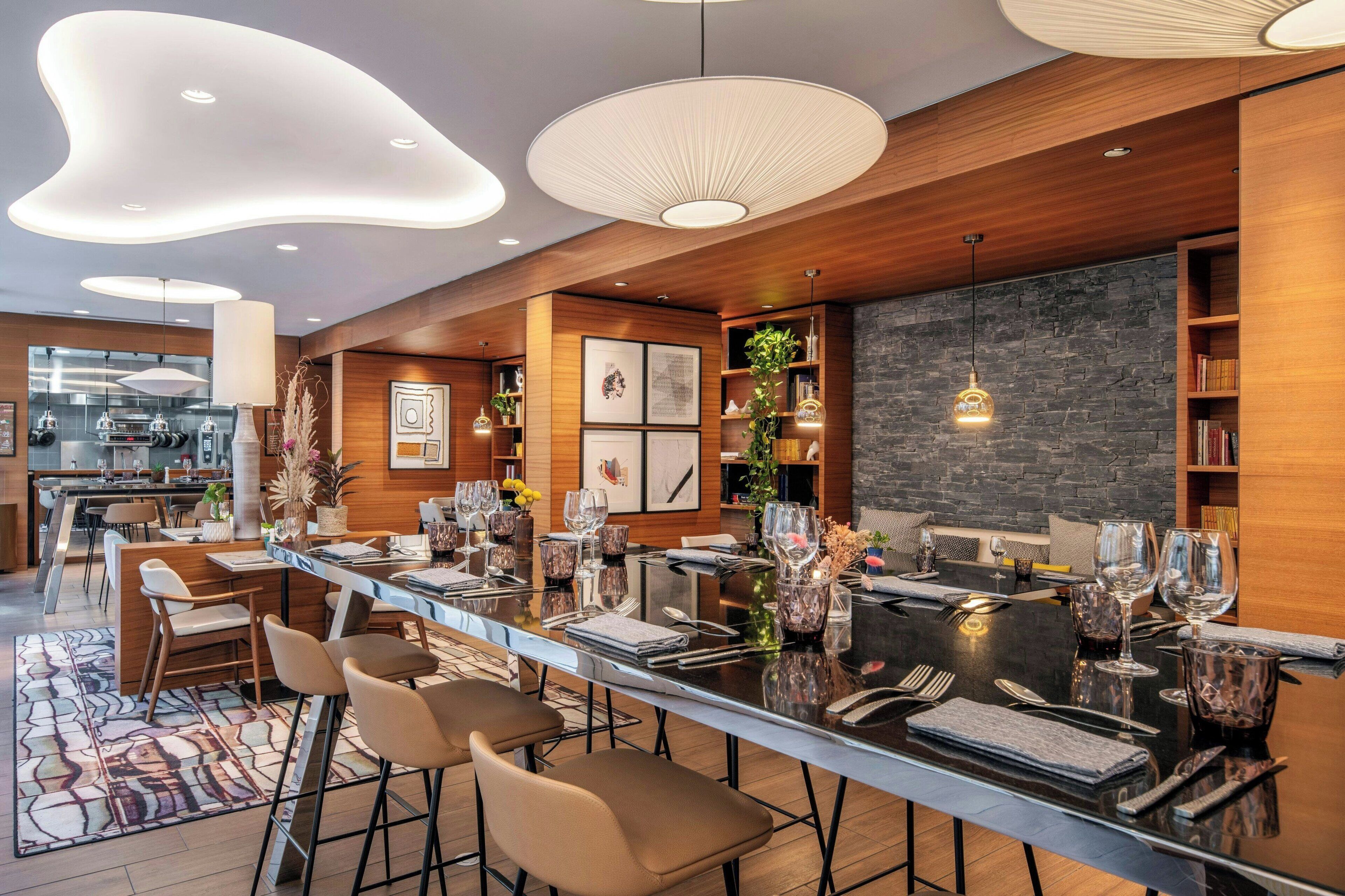A modern dining area with a long table, bar stools, and contemporary lighting fixtures.