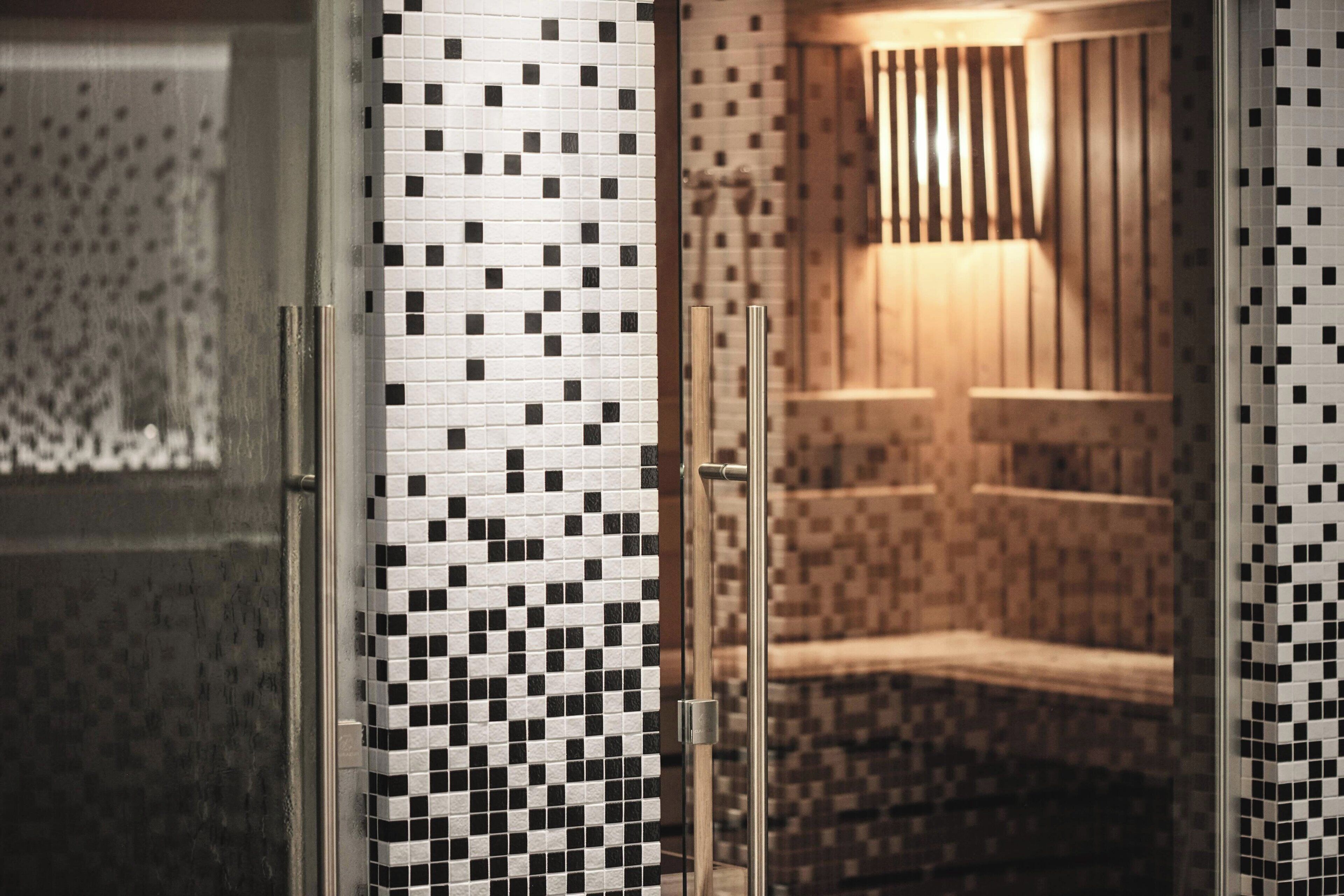 A bathroom with a tiled wall, a glass shower enclosure, and a wooden bench.