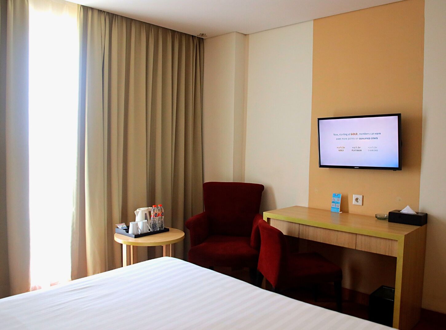 A hotel room with a bed, a desk, a chair, a television, and a window with curtains.