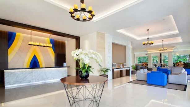 A modern hotel lobby with a reception desk, a round table with a vase of flowers, and a seating area with sofas.