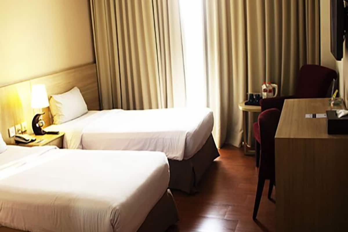 Quarto de hotel com duas camas, uma escrivaninha, uma cadeira, uma TV e cortinas.