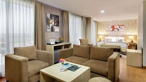 A hotel room with a sofa set, a small table with a vase of flowers, a bed with a white comforter, and a wall-mounted artwork.