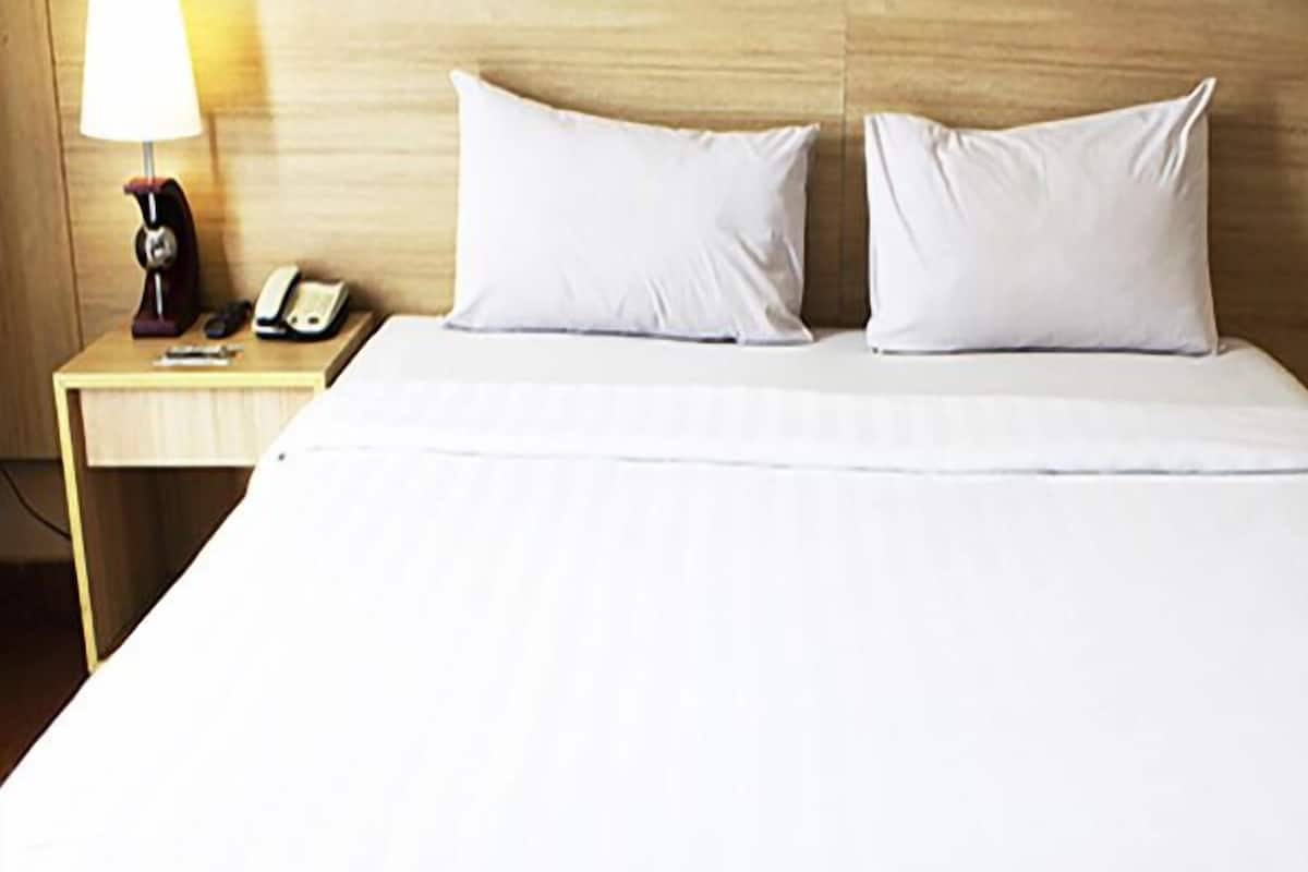 Quarto de hotel com cabeceira de madeira, mesa de cabeceira com abajur, telefone e duas almofadas.