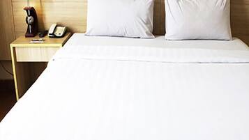 Quarto de hotel com cabeceira de madeira, mesa de cabeceira com abajur, telefone e duas almofadas.